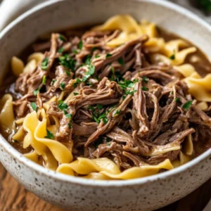 Bowl of Crockpot Beef and Noodles topped with parsley and served with a fork on a light wooden table