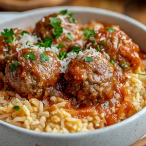 One Pot Meatballs and Rice in a white bowl, garnished with parsley and Parmesan, showcasing rich tomato sauce.