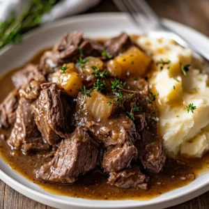 Plate of Slow Cooker Butter Beef drizzled with sauce and garnished with parsley, served with mashed potatoes